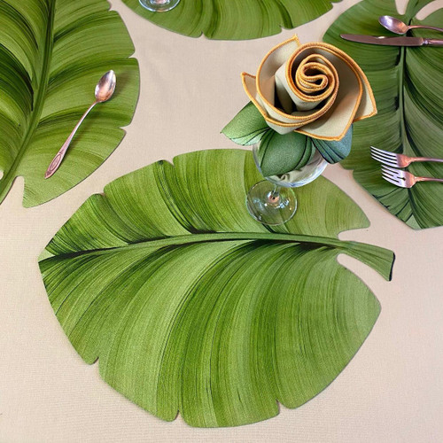 Hand-Painted Palm Leaf Placemat Carole Shiber Designs, a tropical-themed table setting with green palm leaf placemats, a glass vase with a fabric flower, and silverware on a beige tablecloth.