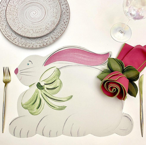 Easter Bunny Carole Shiber Designs, decorative bunny-shaped placemat with pink ears and green bow, placed on a table set with plates, glass, napkins, and cutlery. Easter Bunny Carole Shiber Designs, decorative bunny-shaped placemat with pink ears and green bow, placed on a table set with plates, glass, napkins, and cutlery.