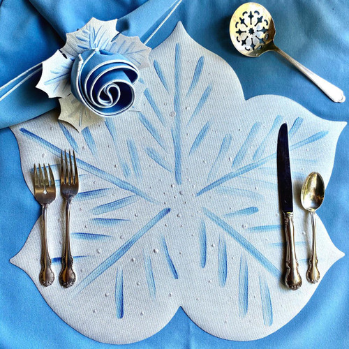 Winter White/Blue Setting Carole Shiber Designs, elegant blue and white table setting with cutlery, a decorative napkin, and a floral motif on a tablecloth.