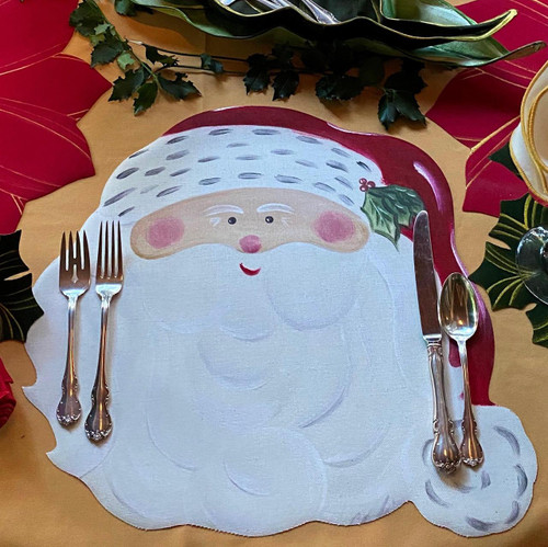 Santa Claus Placemat Carole Shiber Designs, Christmas themed placemat featuring Santa's face with rosy cheeks and a white beard, decorated with holiday foliage around it.