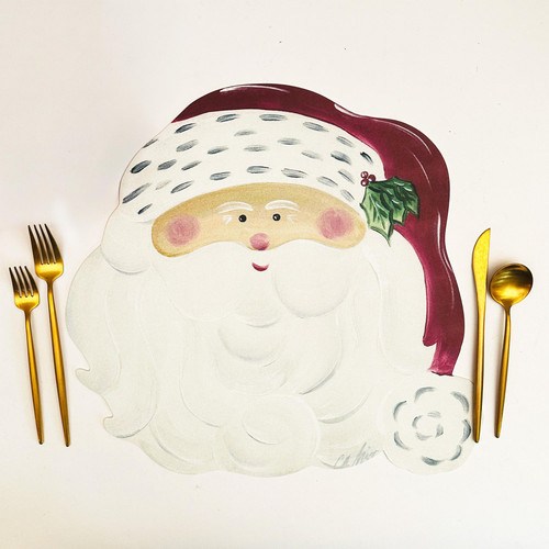 Santa Claus Placemat by Carole Shiber Designs, festive placemat shaped like Santa’s face with a burgundy hat, holly detail, and white beard, displayed with gold cutlery.