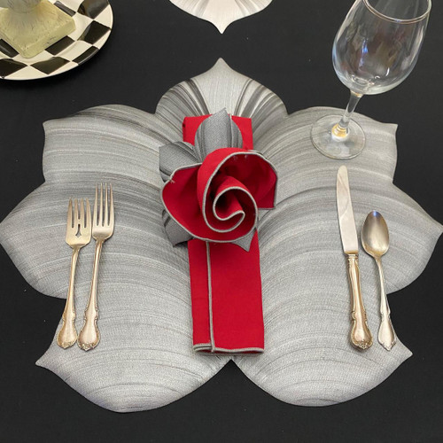 Silver Grey/Black Leaf & Red Carole Shiber Designs, elegant table setting with a silver grey leaf-shaped placemat, gold cutlery, a red and grey fabric napkin folded like a rose, and a wine glass.