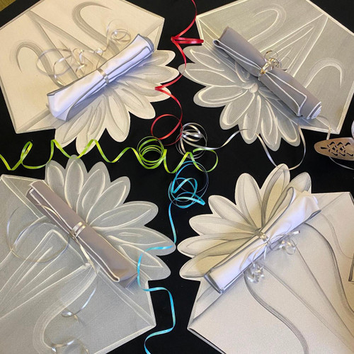 Grey & White Gift Box Party of 4 Carole Shiber Designs, four elegant gift boxes with floral patterns, each decorated with rolled napkins tied with metallic ribbon, surrounded by colorful curling ribbons on a black surface.