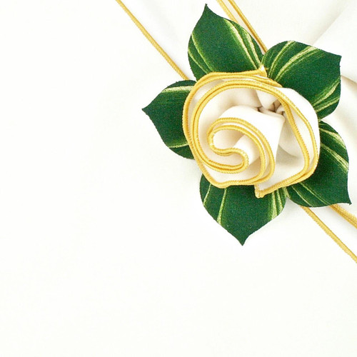 Napkin White/Gold Trim Carole Shiber Designs, an elegant decorative napkin with gold trim designed in a rose shape with green leaves.