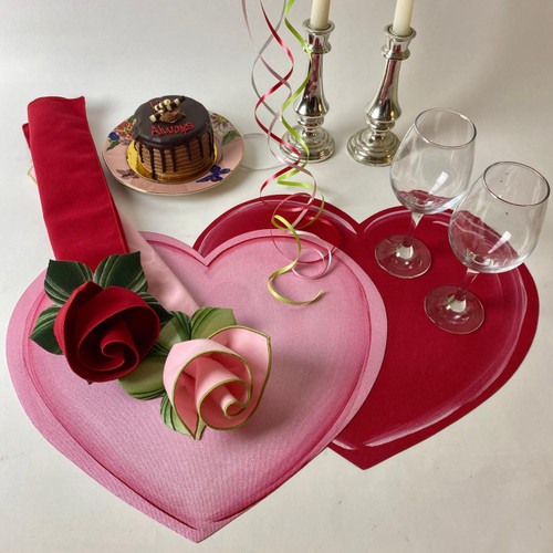Two Hearts Beating As One Carole Shiber Designs, decorative table setting with pink and red heart-shaped placemats, artificial red and pink roses, a chocolate cake with 'Always' written on top, clear wine glasses, silver candlesticks with candles, and colorful ribbon curls for celebration. Two Hearts Beating As One Carole Shiber Designs, decorative table setting with pink and red heart-shaped placemats, artificial red and pink roses, a chocolate cake with 'Always' written on top, clear wine glasses, silver candlesticks with candles, and colorful ribbon curls for celebration.