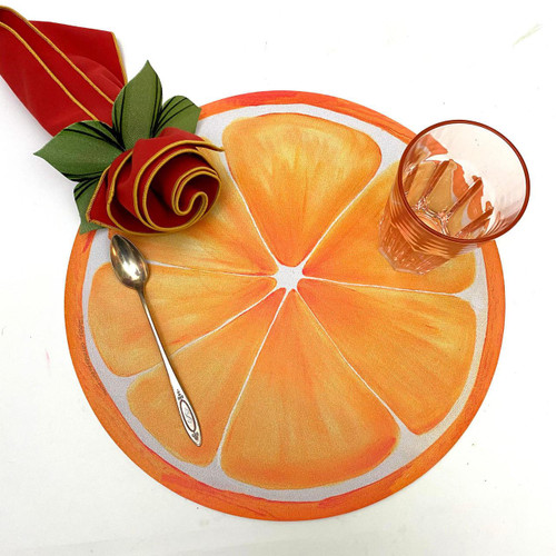 Orange Slice Placemat Carole Shiber Designs, round orange-colored placemat resembling orange slices with a glass of water, a spoon, and a decorative red rose with green leaves on a white background.