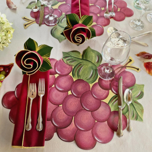 Grapes, Napkin & Leafy Ring Carole Shiber Designs - Decorative table setting with grape-themed design featuring a pink napkin, silver cutlery, and floral accents.