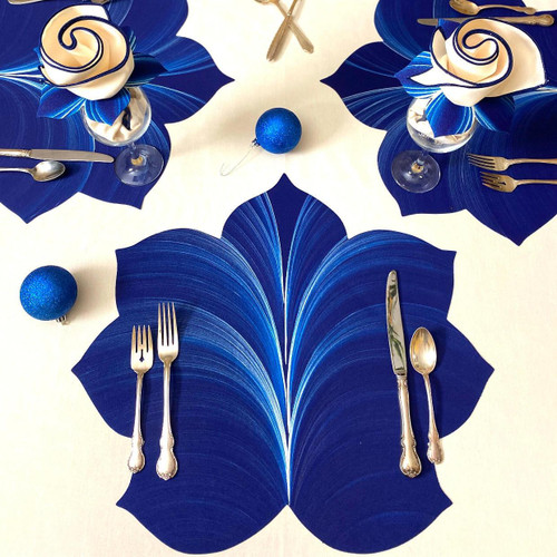 Interlocking Leaf, Deep Blue/Frost Carole Shiber Designs table setting with blue leaf-shaped placemats, blue and white napkins, and silverware, decorated with blue Christmas ornaments, festive and elegant dining decor.