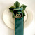 Bouquet Napkin Ring - Pine/Frost, a decorative napkin ring resembling a pine cone with green leaves, on a white plate with embossed design.