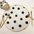 Polka-Dot Round, Black & White Gilt-edged Carole Shiber Designs dining set with black polka dots on a white round placemat, gold flatware, and decorative black and white polka dot napkin.