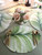 Palm Leaf Placemat by Carole Shiber, a green and white tropical-inspired placemat with a leaf pattern, set on a table with gold cutlery and a floral centerpiece.