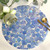 Blue Petals on Round Carole Shiber Designs, a circular decorative piece with painted blue floral petal patterns, topped with a gold-rimmed glass, gold spoon, and pale yellow rolled paper roses. Blue Petals on Round Carole Shiber Designs, a circular decorative piece with painted blue floral petal patterns, topped with a gold-rimmed glass, gold spoon, and pale yellow rolled paper roses.