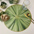 Connecting Leaf Collection Carole Shiber Designs, decorative round table placemat with green leaf pattern and gold accents, paired with glassware and gold cutlery.