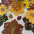 Fall-to-Thanks-to-Everyday Gratitude Carole Shiber Designs, Autumn-themed table decor with a centerpiece of orange and yellow flowers and sunflower-themed placemats with gold utensils.