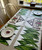 Winter Mountain Village, S/6 Carole Shiber Designs table runner set with green palm leaf pattern and barnyard scene on fabric, displayed on a dining table.