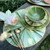 Complete 6-Piece Botanic Place-Setting, botanical-themed dinnerware with green leaf patterns and gold accents, including plates, bowls, and gold utensils.