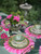 Pink Daisies & Green Leaves S/4, a set of floral dinnerware and table decor featuring pink daisies and green leaves in a glass vase, with matching plates, bowls, glassware, and gold utensils on a vibrant pink and green table setting. Pink Daisies & Green Leaves S/4, a set of floral dinnerware and table decor featuring pink daisies and green leaves in a glass vase, with matching plates, bowls, glassware, and gold utensils on a vibrant pink and green table setting.