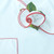 White with Red Trim Carole Shiber Designs, close-up of a decorative fabric flower with white petals, red-trimmed edges, and green leaves.