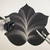 5 Point Fountain Leaf - Black with Silver Carole Shiber Designs, decorative leaf-shaped table mat with silver detailing, accompanied by a black and silver fabric flower, a silver knife and spoon on a white surface.