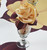 7 Point Leaf - Eggplant/Gold & Bronze Carole Shiber Designs, decorative napkin folded into a rose shape in a glass vase, with a leaf-shaped tablecloth underneath.