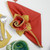 7 Point Leaf - Gold/Copper & Bronze Carole Shiber Designs, an elegant folded red napkin with a decorative silk flower in gold and copper tones.