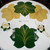 7 Point Leaf - Pine/Gold & Bronze Carole Shiber Designs, decorative table setting with leaf-shaped placemats in green and yellow, and matching napkin and flower-shaped napkin rings.
