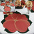 7 Point Leaf - Pine/Gold & Bronze Carole Shiber Designs, a decorative table setting with a large red poinsettia leaf placemat with gold accents, complemented by matching floral napkins arranged in a glass, and a poinsettia-themed tablecloth.