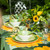 Wild Sunflower Tablescape Carole Shiber Designs, vibrant table setting with sunflower-themed plates, bowls, and cutlery accompanied by a floral centerpiece of yellow flowers and green foliage.