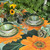 Wild Sunflower Tablescape Carole Shiber Designs, a table setting featuring sunflower-themed dinnerware with green and orange leaves, surrounded by fresh flowers and lush green foliage.