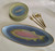 Rainbow Trout 7-Pc. Entertainer's Set, fish-themed dinnerware including a large oval platter and a stack of smaller plates, along with gold-colored cutlery including two forks, a knife, and a spoon, designed for serving and entertaining.