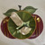 Cherries Placemat, decorative placemat designed to resemble cherry motifs with green leaves and red background, set with gold utensils and napkins.