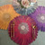 Jeweltone Mums, colorful paper placemats in orange, red, purple, and blue with floral patterns, arranged on a table with gold cutlery and a white floral centerpiece.
