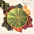 Swirling Leaves Placemat, decorative green leaf-themed table mat with gold edging, arranged with gold cutlery, a wine glass, and a flower napkin on a table with autumn-colored leaf-shaped placemats.