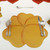 Buttercup Placemat - Gold Carole Shiber Designs, a yellow and gold flower-shaped placemat on a white table setting with silver flatware.