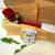 Our $100 Gift Certificate Carole Shiber Designs, image of a gift certificate with a decorative illustration of a door with wreaths, a red fabric rose, and green leaves on a white surface.