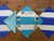 Squares 'n Stripes Set of 4 Carole Shiber Designs napkins and table settings with blue and white striped pattern, a light blue folded napkin, cutlery, a wine glass, and a wooden table.