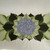 Carole Shiber Hydrangea Pacemat, a decorative design featuring a vibrant cluster of purple hydrangea flowers surrounded by green and black stylized leaves.