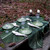 Vintage Leaf Topper Carole Shiber Designs, elegant table setting with green leaf-themed plates, white napkins, wine glasses, and candles on a natural outdoor wood surface. Vintage Leaf Topper Carole Shiber Designs, elegant table setting with green leaf-themed plates, white napkins, wine glasses, and candles on a natural outdoor wood surface.