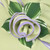 HoneyDew with Lilac Trim Napkin Carole Shiber Designs, close-up of a decorative napkin with a fabric rose and lilac-colored trim, green and white leaves in the background.