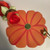 Popping Orange Poppy, LIMITED EDITION Carole Shiber Designs, a vibrant decorative item resembling a pumpkin with orange petals and green accents, displayed with a red ribbon and gold-handled tool.