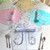 Complete Party of 4 Carole Shiber Designs, colorful flower-shaped tableware placemats with matching napkins and clear wine glasses, set for a festive occasion.