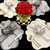 Grey & Buttercream Buttercups 4 Set Carole Shiber Designs, elegant table setting with cream and grey flower-shaped placemats, gold cutlery, and decorative napkins with bows, centered by a bouquet of red roses and green berries in a black and white checkered vase.