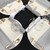 Moonscape Setting Grey & White Carole Shiber Designs, elegant table setting with grey and white napkins, glassware, and gold cutlery arranged on a white tablecloth with black and white circular placemats.