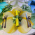 Lily Placemat, Yellow - Carole Shiber Designs; image shows a vibrant yellow lily-shaped placemat on a dining table, decorated with green and yellow napkins, glassware, and silver cutlery.