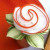 White with Orange Trim Napkin Carole Shiber Designs, a decorative napkin crafted to resemble a flower with swirling white and orange edges and green leaf accents.