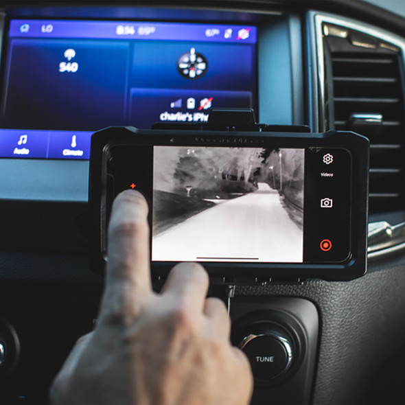 Interior vehicle view of a user operating the NightRide 360 thermal camera interface on a dashboard mounted mobile device