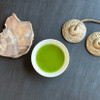 Cup of ceremonial matcha on a black table with chimes and a piece of petrified wood