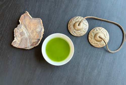 cup of ceremonial matcha on a black table with chimes and a peice of petrified wood