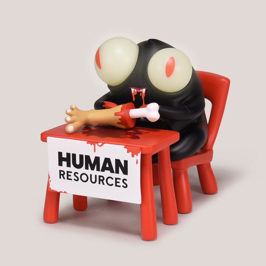 Black monster figure with yellowish eyes and red slit pupils sits in a red chair behind a desk that says Human Resources. There is a severed foot on the desk.