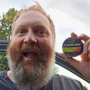 Smiling customer holding a FlowBlend Dewdrop Apple CBD pouch can next to his truck